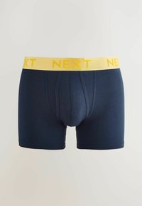 Tengerészkék pamut boxer sort sárga elasztikus derékkal, amelyen a "NEXT" felirat található. Elöl zsebes és jól illeszkedő kialakítás jellemzi.