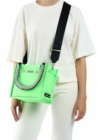 Groene stoffen tas met een gewatteerd ontwerp, voorzien van een gevlochten handvat en zilveren hardware. De tas heeft een afneembare zwarte schouderband.