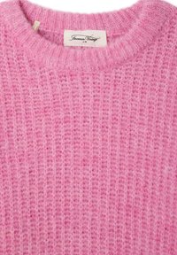 Ružový pletený sveter s textúrovaným vzorom, okrúhlym výstrihom a mäkkučkým, chmýriacim povrchom. Štítok viditeľný na výstrihu.
