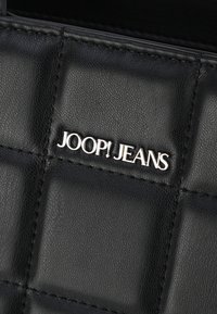 Czarna skórzana torebka z pikowanym wzorem, srebrnym logo "JOOP! JEANS" oraz drobnymi detalami szycia. Gładka tekstura i wyraźnie zarysowany kształt.