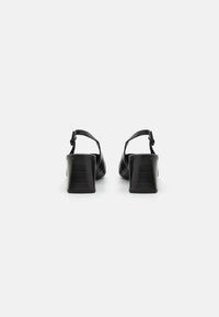 Black leather heeled sandals with a chunky heel, featuring an adjustable ankle strap and smooth texture; minimalist design with a closed back.