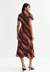 Vestido midi negro con estampado floral, de mangas cortas, presenta patrones de flores rojas y rosas, cintura ajustada y dobladillo acampanado. Combinado con zapatos de tacón negros.