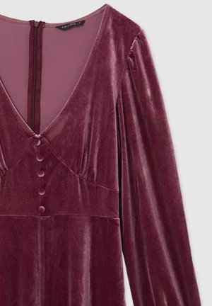 Abito in velluto bordeaux con scollatura profonda a V, maniche lunghe e bottoni decorativi al centro. Tessuto morbido e silhouette elegante.