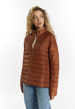 Roestkleurige pufferjack met een ritssluiting aan de voorkant, gewatteerde textuur en hoge kraag. Gepaard met lichtblauwe jeans, op een witte achtergrond.