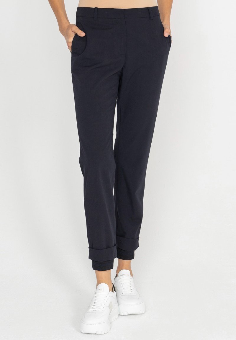 Granatowe spodnie z dopasowanym krojem, z podwiniętymi mankietami, zawierające dwie kieszenie po bokach oraz gładką fakturę, zestawione z białymi trampkami na platformie.