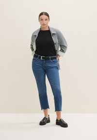 Szary żakiet zapinany na guziki na czarną koszulę, niebieskie dżinsy z poszarpanymi nogawkami i czarne buty. Outfit charakteryzuje się klasyczną, casualową sylwetką.