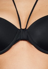 Svart push-up bikini-top med glatt stoff, flettet nakkestropp og knutedetalj mellom koppene; designet for støtte og komfort.