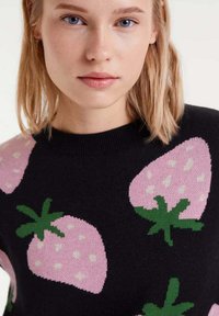 Suéter de punto en negro con grandes patrones de fresas rosa y hojas verdes. Presenta un cuello redondo y una textura suave.