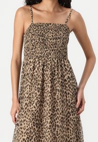 Robe imprimée léopard avec un corsage smocké, de fines bretelles spaghetti et une jupe fluide. Le tissu présente une texture douce dans des tons de brun et de noir.