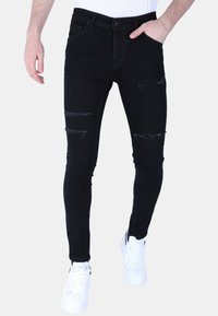 Zwarte skinny jeans met gescheurde details op de knieën, gemaakt van denim. Gecombineerd met witte sneakers, die een minimalistisch ontwerp tonen.