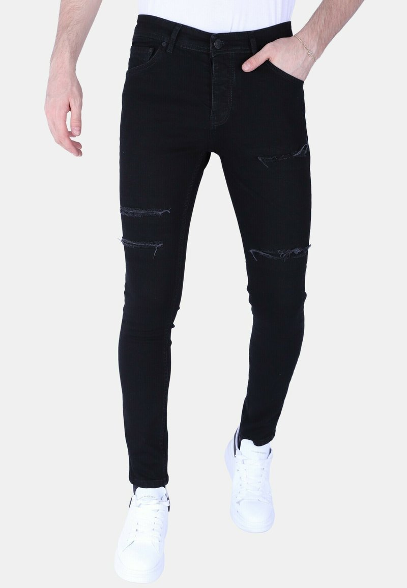Zwarte skinny jeans met gescheurde details op de knieën, gemaakt van denim. Gecombineerd met witte sneakers, die een minimalistisch ontwerp tonen.
