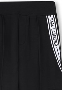 Zwarte broeken van een textuurstof, met een witte streep langs de zijkant waarop "KARL LAGERFELD" in vetgedrukte letters is afgebeeld.