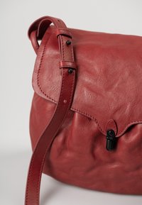Borsa a spalla in pelle rossa con finitura testurizzata, chiusura a patta e tracolla regolabile. Presenta dettagli in hardware nero e cuciture decorative.