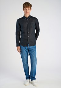 Camicia nera a maniche lunghe con bottoni e tasca, abbinata a jeans in denim blu e sneaker bianche. Design semplice, texture liscia.