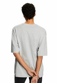Grå kortärmad t-shirt med rund halsringning, avslappnad passform och mjukt material, sedd bakifrån med armarna korsade bakom ryggen.