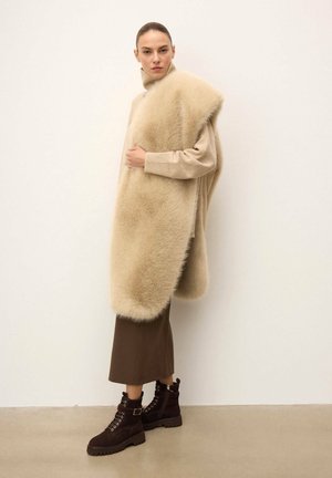 Beige gebreide trui met een bontkraag, gecombineerd met een bruine rok en donkerbruine veterlaarzen. Soepele textuur en gelaagd ontwerp.