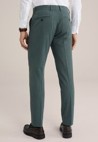 Finoman textúrázott, egyenes szabású, zöld nadrág, melyen két hátulsó zseb található gombos záródással. Sötét cipővel viselve.