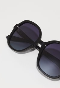 Black oversized sunglasses with gradient dark to light purple lenses and a glossy plastic frame. Features a subtle bridge cutout detail.