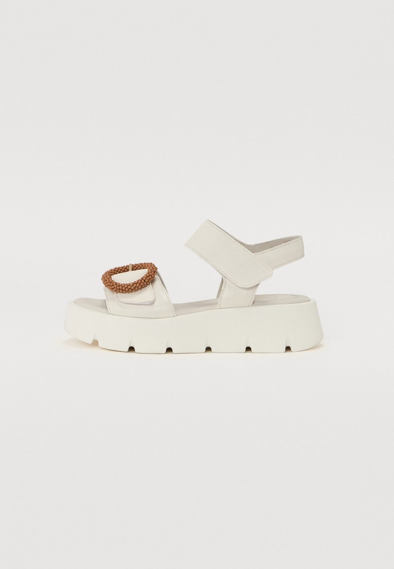 White platform sandals with a textured upper, adjustable cross-strap, and a round, woven brown accent on the instep. Chunky sole design.