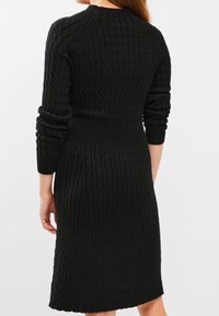 Robe tricotée noire avec un motif en câble texturé, silhouette ajustée, manches longues et col rond, s'étendant jusqu'à la mi-mollet.