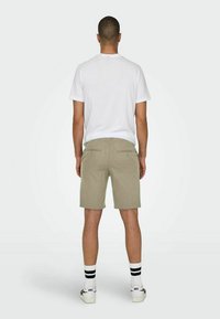 Pantaloni corti khaki con una texture liscia, due tasche posteriori e un semplice design a vita alta. Indossati con una maglietta bianca e calze a righe.