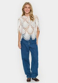 Top in pizzo bianco con motivi aperti intricati, maniche corte e scollo con fiocco, abbinato a pantaloni in denim blu a vita alta.