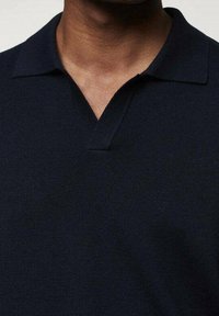 Námořnická pletená polo košile s límečkem a výstřihem ve tvaru "V". Látka má hladkou strukturu, vhodnou pro volnočasové nošení.