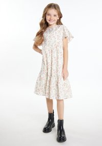 Blumenkleid mit kurzen Ärmeln, gerafftem Taillenbund und gestuftem Rock in Off-White mit rosa und grünen Mustern. Kombiniert mit schwarzen Knöchelstiefeln.