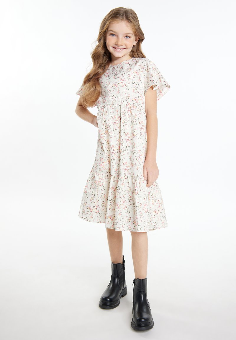 Blumenkleid mit kurzen Ärmeln, gerafftem Taillenbund und gestuftem Rock in Off-White mit rosa und grünen Mustern. Kombiniert mit schwarzen Knöchelstiefeln.