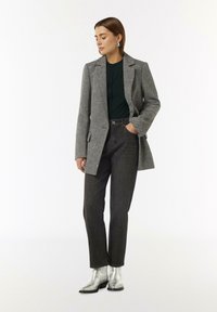 Blazer grigio con texture e vestibilità su misura, abbinato a jeans scuri a vita alta e stivaletti con tacco in argento lucido. Sotto una semplice maglietta verde.