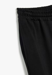 Zwarte sweatpants met een elastische tailleband en zijzakken, gemaakt van zacht, glad materiaal, met scherpe lijnen en minimale stiksels.