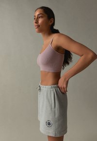 Reggiseno sportivo rosa chiaro a coste abbinato a pantaloncini grigi con coulisse, tasche laterali e dettaglio logo blu navy. Morbido cotone.