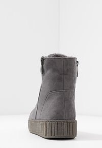 Bottine en daim gris avec doublure en fausse fourrure, dotée d'une fermeture éclair latérale et d'une semelle en caoutchouc texturée avec des rainures verticales.