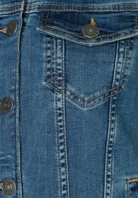 Denimjack met een blauwe kleur, drukknoopjes, dubbele borstzakken en contrasterende oranje stiksels. Gestructureerde stof met zichtbare naden.