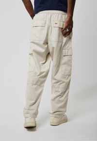 Pantalons cargo beige clair avec une coupe décontractée. Comprend plusieurs poches, une taille élastique et un design minimaliste. Tissu texturé.