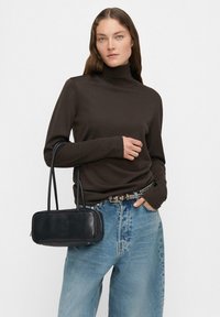 Brązowy sweter z golfem, niebieskie luźne dżinsy, pasek z srebrnymi ćwiekami oraz czarna prostokątna torebka na podwójnych paskach. Minimalistyczny design, gładka tekstura.