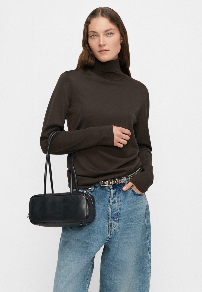 Brązowy sweter z golfem, niebieskie luźne dżinsy, pasek z srebrnymi ćwiekami oraz czarna prostokątna torebka na podwójnych paskach. Minimalistyczny design, gładka tekstura.