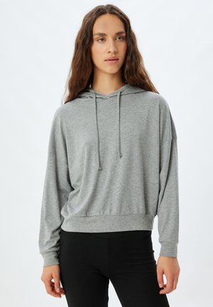 Sudadera gris de manga larga con un ajuste relajado, cordones en el cuello y dobladillo acanalado. Combinada con leggings negros, textura de tela suave.