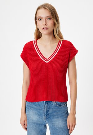 Top corto de punto rojo con cuello en V y acentos de rayas blancas a lo largo del escote, combinado con jeans de mezclilla azules.