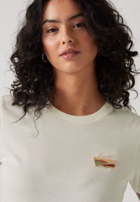 Krämfärgad bomulls-t-shirt med rund hals och korta ärmar, med en broderad flerfärgad Levi's logotyp på bröstet.