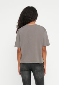 Grå kortermet t-skjorte med avslappet passform, rund hals og sømdetaljer, parret med svarte jeans med subtil tekstur.
