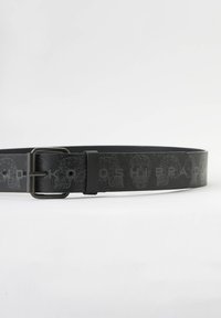 Zwarte synthetische riem met een geometrisch schedelpatroon. Voorzien van een metalen gesp en een gladde textuur. Maat- en merkdetails zijn niet zichtbaar.