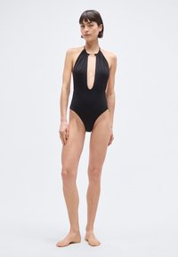 Μαύρο ολόσωμο μαγιό με βαθύ V ντεκολτέ, τιράντες χιαστί και υφή υφάσματος. Διαθέτει χρυσή λεπτομέρεια στο λαιμό.