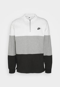 Nike-pullover med en kvart dragkedja, med vita, grå och svarta färgblock. Gjord av mjukt material, med en liten Nike-logga på bröstet.