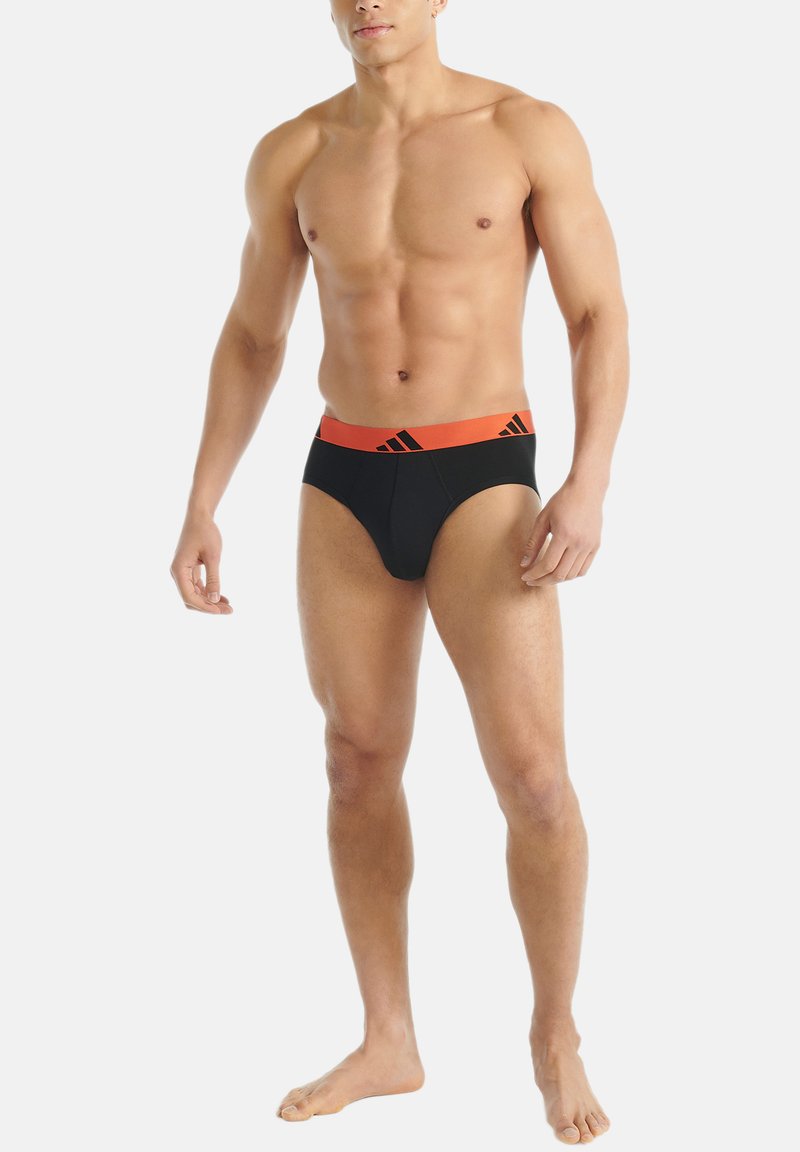Mustat vyötäröluun alushousut oranssilla Adidas-logolla. Istuva muotoilu, joustavasta kankaasta valmistettu, sileä pinta, keskikorkea vyötärö.