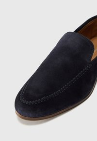 Marineblaue Wildleder Slipper mit glatter Textur, runder Zehenform und kontrastierenden Nähten entlang der Kante. Leichte Gummisohle.
