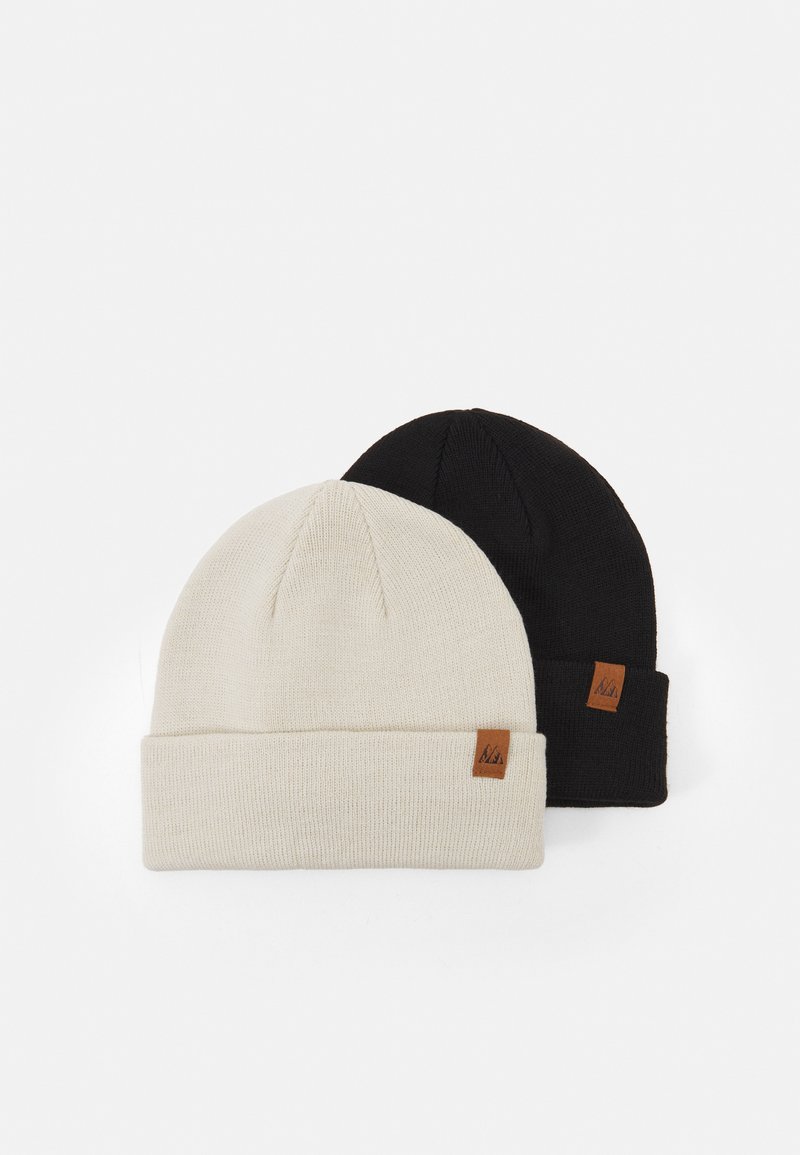 Dos gorros: uno crema y otro negro. Ambos son de punto, con un dobladillo y una pequeña etiqueta de logo marrón en el costado, mostrando detalles de textura y diseño.