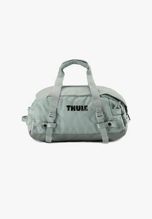 Sac de sport gris avec une finition brillante, doté de poignées supérieures doubles, d'une sangle latérale et d'un logo à l'avant. Le matériau semble durable et résistant à l'eau.
