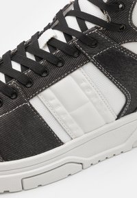 Kotníková teniska s horní částí z černého denimu a bílého textilu, černými tkaničkami a strukturovanou bílou gumovou podrážkou s jemným vzorem.