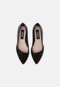 Black pointed-toe flats with a suede front and smooth leather sides. Interior features a light tan insole with the brand name ZIGN.